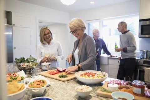 Senior couples preparing dinner and drinking wine in kitchen Stock Photos