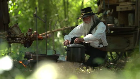 A senior cowboy preparing food at a rustic outdoor campfire Vídeos de archivo 326210726