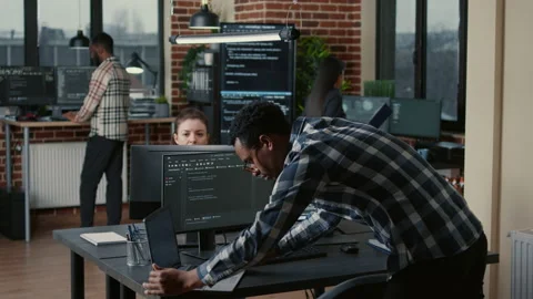 Senior developer coding on laptop at desk with computer screens parsing code Stock Footage 168247709