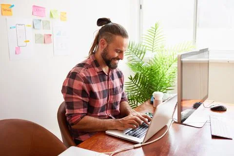Senior developer works in open plan creative office, man bun hipster look Stock Photos