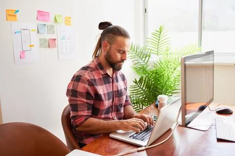 Senior developer works in open plan creative office, man bun hipster look 스톡 사진