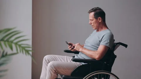 Senior disabled man in wheelchair using smartphone, checking messages, watching Stock Footage 219480230