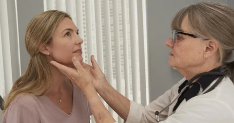 Senior doctor feeling lymph nodes on female Caucasian patient in exam room Stock Footage 102770565