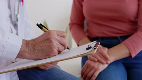 Senior doctor making notes while talking with female patient at medical room Stock Footage 277466839