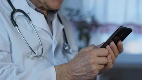 Senior doctor in white uniform using smartphone in hands Stock Footage 220706855