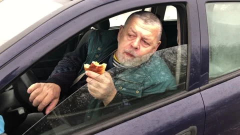 Senior driver eating patty while sitting inside his car 스톡 동영상 144976064