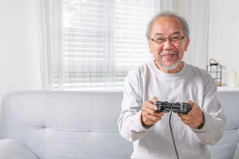 Senior elderly laughing on sofa using controller play game Stock Photos