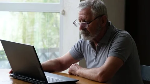 Senior elderly man in glasses sitting at the table and looking at laptop Stock Footage 170002146
