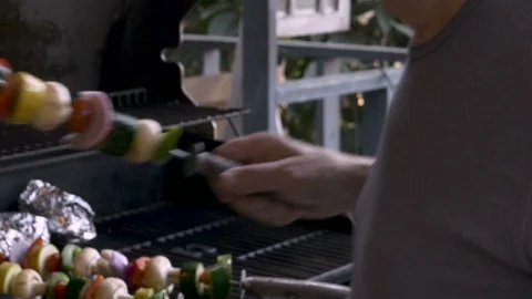 Senior elderly man in his 70s placing healthy veggie shish kebabs on a hot bbq Stock Footage 86001929
