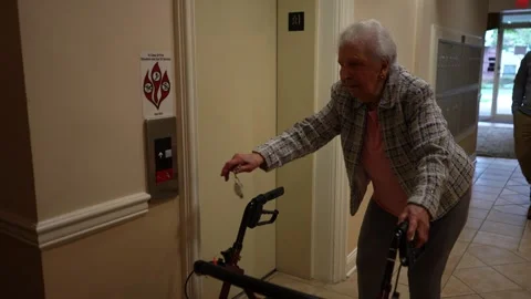 Senior elderly old mother using a walker walking to elevator in nursing home Stock Footage 253565813