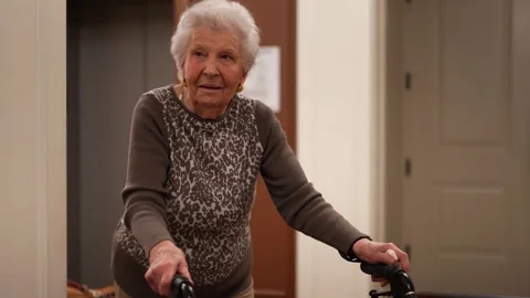 Senior elderly old mother using a walker walking to elevator in nursing home Stock Footage 267857598