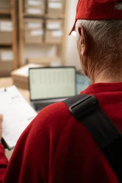 Senior elderly postal worker using a digital tablet to check parcel boxes in  Stock Photos
