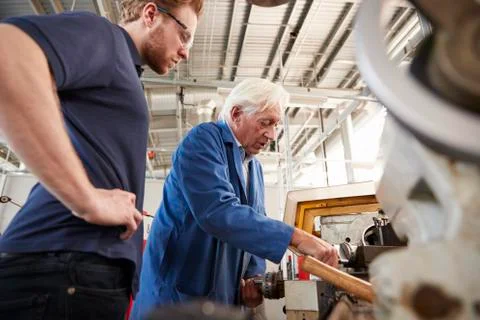 Senior engineer demonstrating equipment to apprentice at machine bench, low Stock Photos