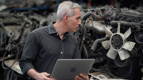 Senior engineer using laptop computer checking list old used car engine in ma Stock Footage 153568741