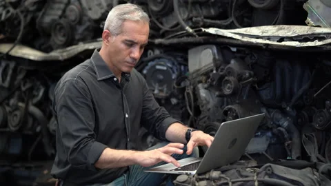 Senior engineer using laptop computer checking list old used car engine in ma Stock Footage 153569107