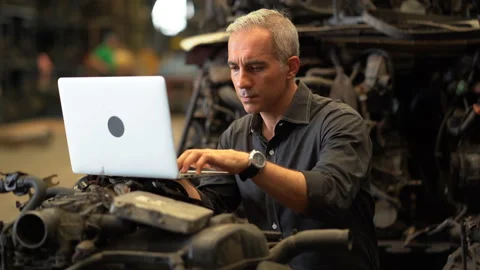 Senior engineer using laptop computer checking list old used car engine in ma Stock Footage 153569111