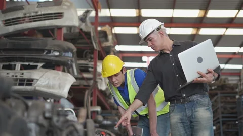 Senior engineer using laptop computer checking list old used car engine with Stock Footage 153570529