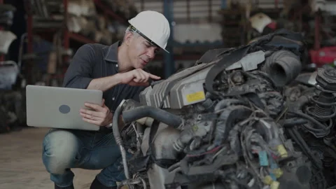 Senior engineer using laptop computer checking list old used car engine in ma Stock Footage 153571663