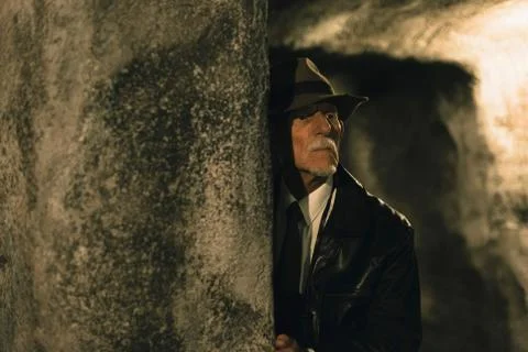 Senior explorer with hat in dark cave inspecting environment. Stock Photos