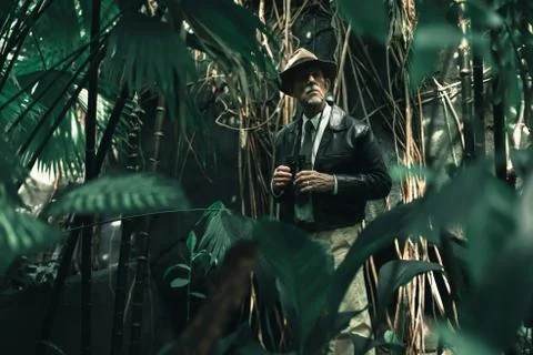 Senior explorer standing in dense jungle looking carefully. Stock Photos