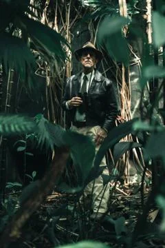Senior explorer standing in dense jungle looking carefully. Stock Photos