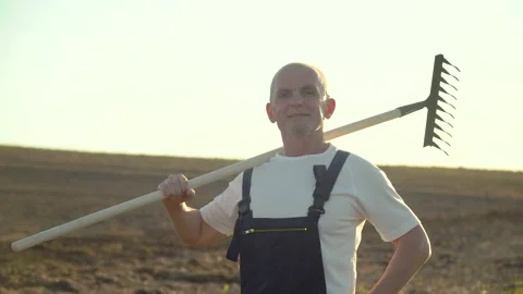 A senior farmer standing through a field with rake. Farming and agriculture Stock Footage 135999799