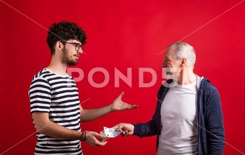 Senior father giving money to his son in a studio on red background. Stock-Fotos