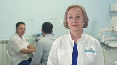 Senior female doctor looking at camera while male doctor talking to patient on Stock Footage