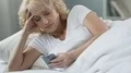 Senior female lying in bed, holding cellphone and smiling, message from beloved HD Footage