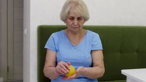 Senior female performs hand therapy with spiky exercise ball indoors Video stock 331053052