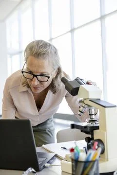 Senior female scientist using microscope and laptop 스톡 사진