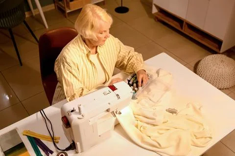 Senior female tailor with thread spools and sewing machine in atelier at nigh Stock Photos