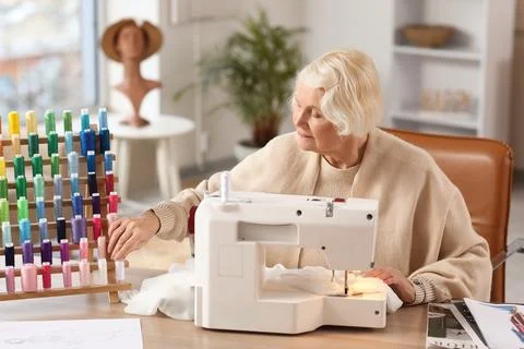 Senior female tailor with thread spools and sewing machine at table in atelie Stock Photos