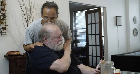 Senior Gay Man Using Smart Phone as Husband Walks in and Kisses Him Stock Footage 111497443