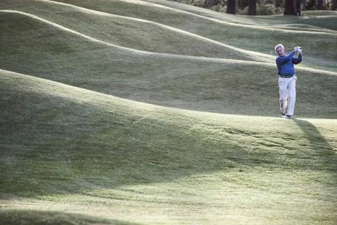 Senior golfer hitting a second shot from the fairway of a golf course. Stock Photos
