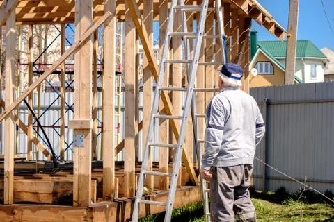 Senior gray-haired builder inspects the frame of a standing country house Stock Photos