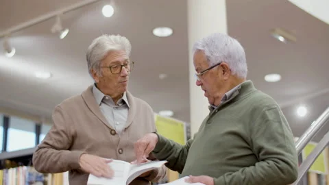 Senior gray-haired friends discussing book in public library Stock-Footage 232620682