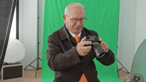 Senior grey haired man holding dslr camera with hands adjusts lens in studi.. Stock Footage 339198776
