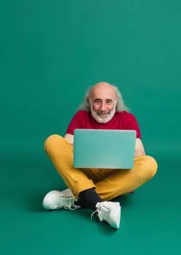 Senior grey-haired man using laptop isolated over green background. Stock Photos