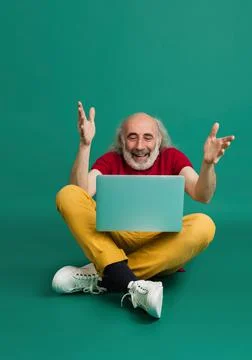 Senior grey-haired man using laptop isolated over green background. Stock Photos