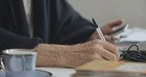 Senior Hands Writing Notes and Using Smartphone Demonstrating Multitasking Video stock 344348368
