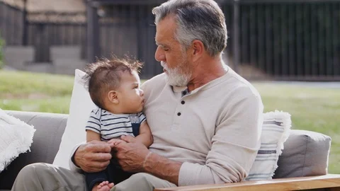 Senior Hispanic man sitting on a seat in the garden with his baby grandson on Stock Footage