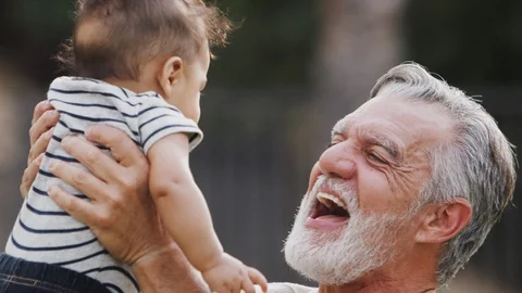 Senior Hispanic man talking to his baby grandson, holding him in the air, close Stock Footage