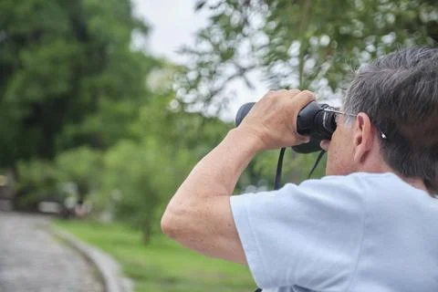 Senior Hispanic man using binoculars to spot birds as a hobby in an urban par Stock Photos