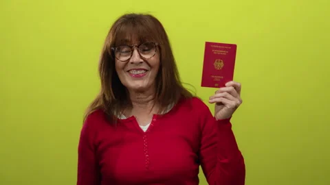 Senior hispanic woman smiling while holding a german passport against a vib.. Stock Footage 311947089