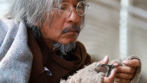 Senior homeless cutting nails using nail clipper on street.  Stock Footage 101387728