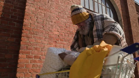 Senior Homeless Man Sorting Items in Shopping Cart on City Street Stock Footage 345707209