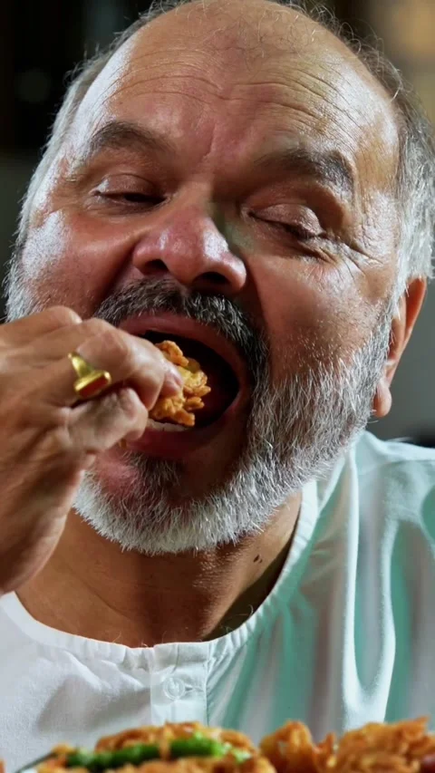 Senior Indian man sitting with snacks, reacting joyfully to tasty Video stock 343106932