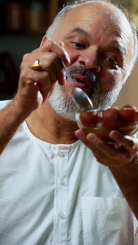 Senior Indian man sitting with snacks, reacting joyfully to tasty Stock-Footage 343106993