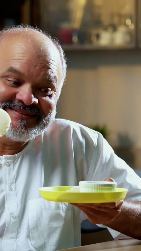 Senior Indian man sitting with snacks, reacting joyfully to tasty Stock Footage 343106994